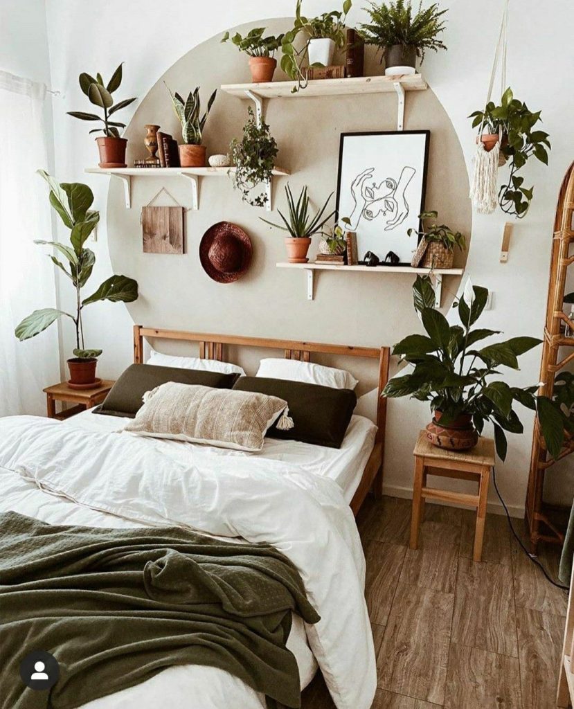 Earthy boho bedroom with a large painted circle arch on a cream wall above the bed, styled with two floating white shelves filled with terracotta plant pots, books, and trailing greenery.