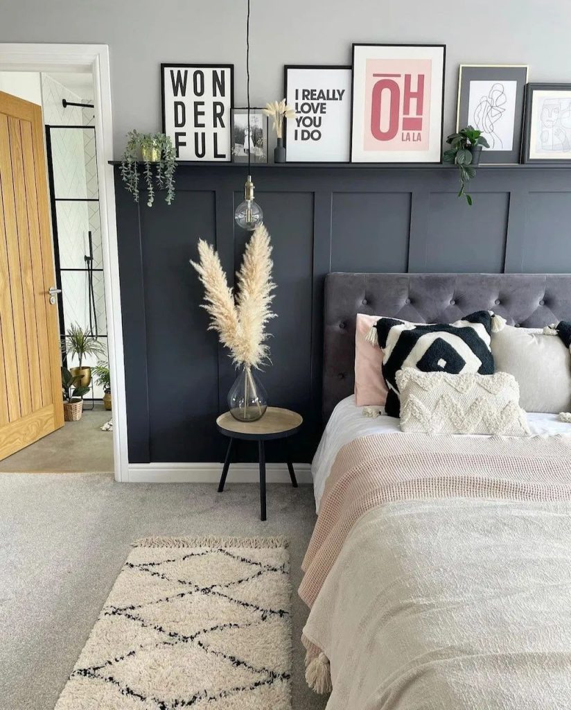 Dramatic bedroom with a dark navy board and batten feature wall and a slim black picture ledge shelf styled with mixed framed typography and line art prints, pampas grass, and trailing plants.