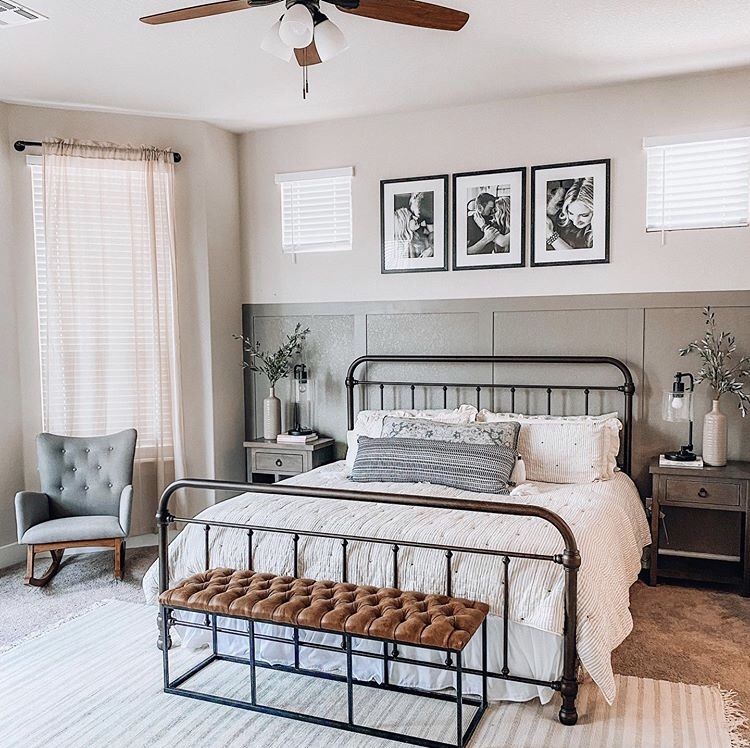 Farmhouse master bedroom with a half wall board and batten feature in sage grey, three matching large black framed black and white personal photos above the bed hung in a horizontal row, and a black iron bed frame.