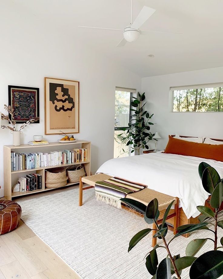 Boho bedroom with white bedding, terracotta pillow, low bookshelf, and rubber plant