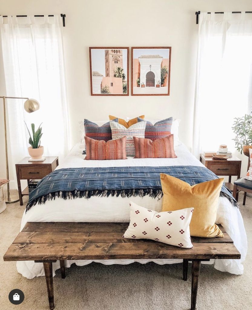 Boho bedroom with Moroccan-inspired art prints above the bed, layered ethnic cushions, and a wooden bench