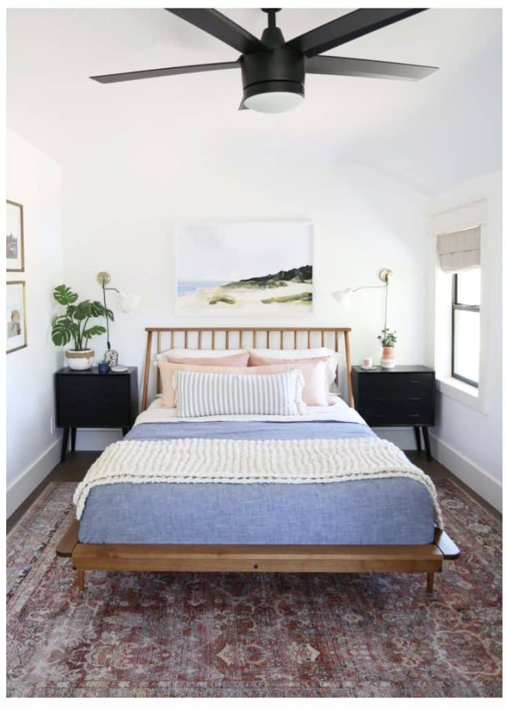 Boho bedroom with a wooden spindle bed frame, large landscape artwork, and black nightstands