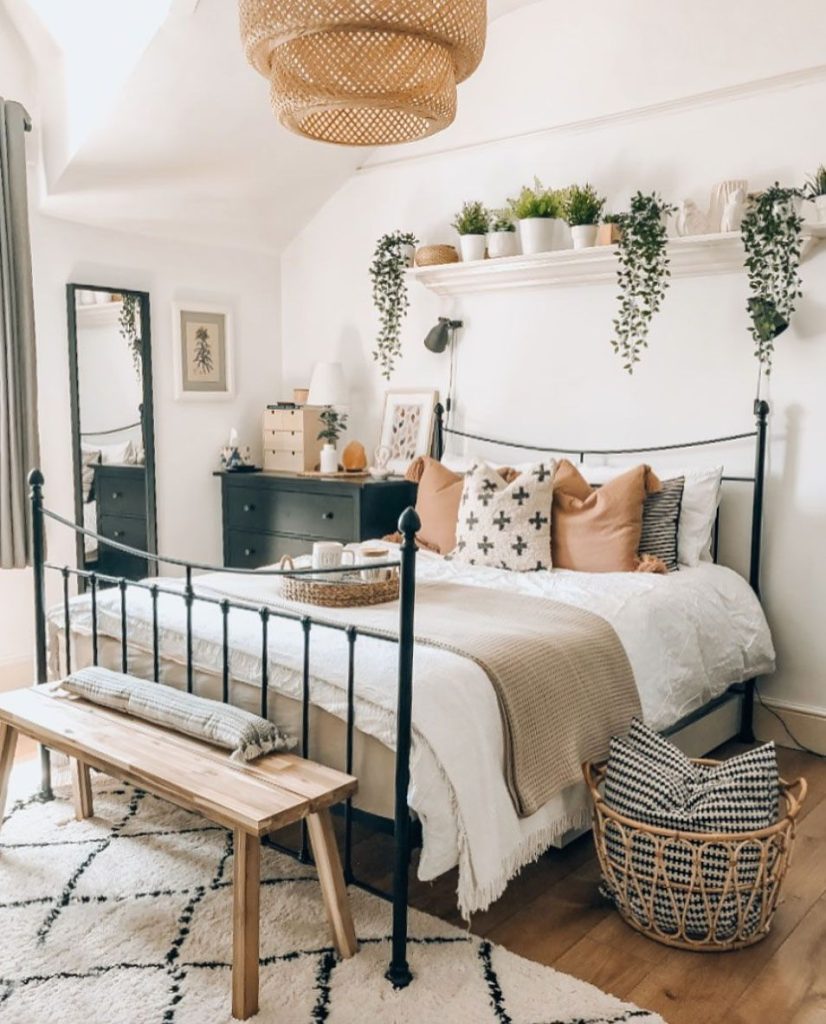 Boho bedroom with a decorative mantel shelf filled with trailing plants above a black iron bed frame