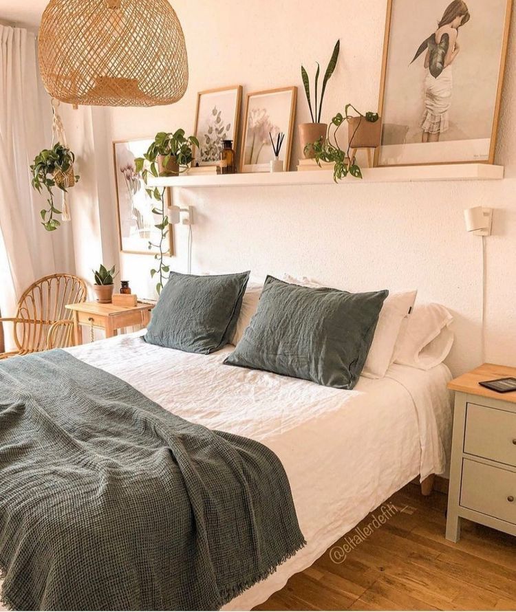 Small boho bedroom with a ledge shelf styled with framed art and plants above the bed, rattan pendant light, and sage green bedding