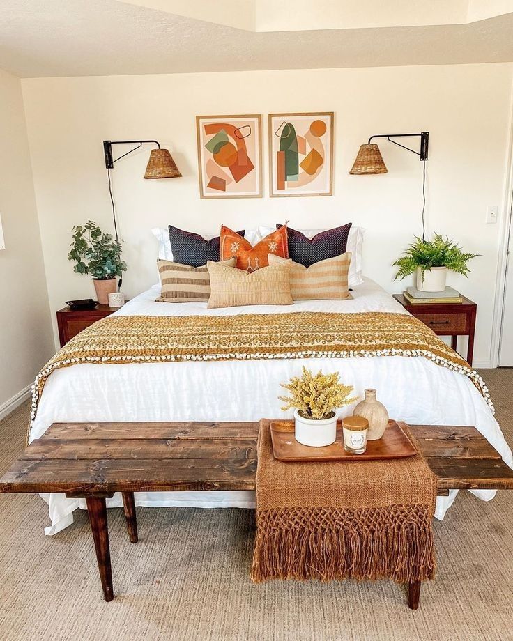 Boho bedroom with layered pillows in terracotta and earth tones, rattan wall sconces, and abstract art