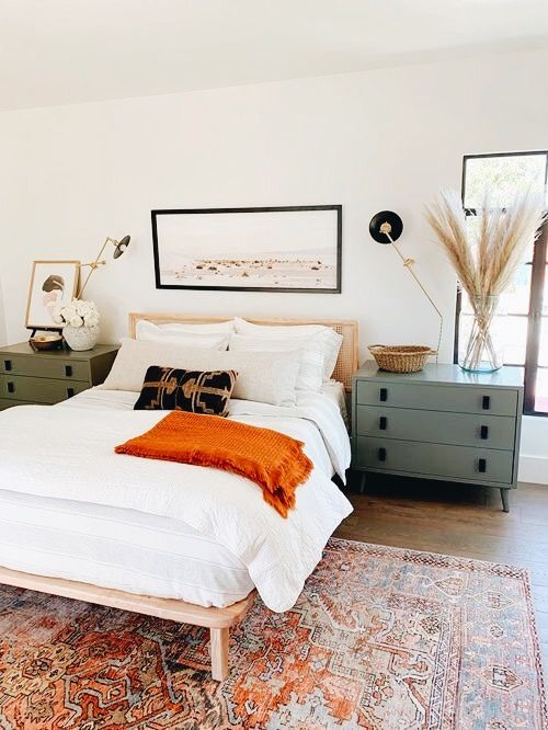 Boho bedroom with pampas grass in a glass vase, cane headboard, and vintage orange rug
