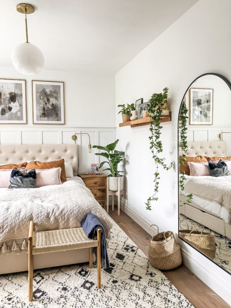 Boho bedroom with a large arched black floor mirror, rattan bench, woven basket, and trailing ivy plant