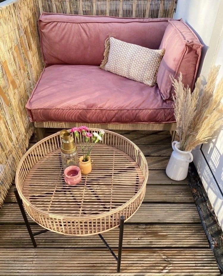 Small balcony with dusty pink sofa, bamboo screen, round rattan coffee table and pampas grass in white vase