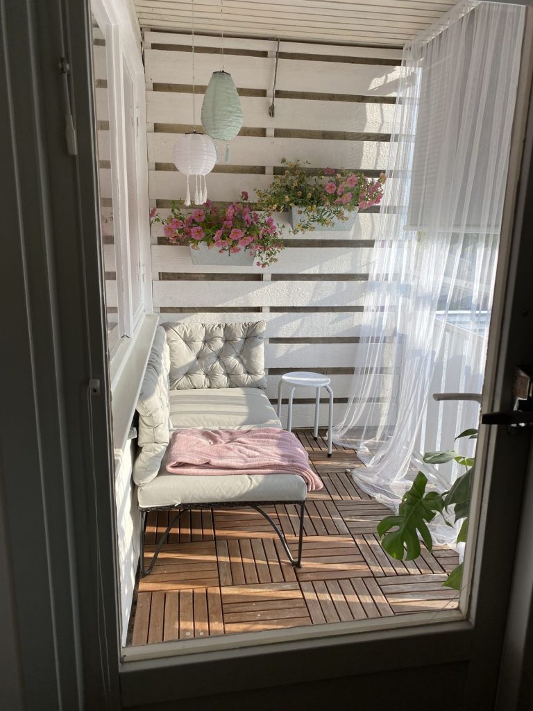 Small balcony with white shiplap privacy screen, window box flowers, hanging paper lanterns and sheer curtains