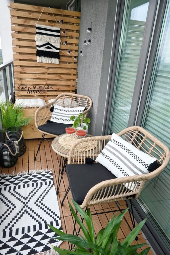 Boho small balcony with rattan egg chairs, wooden pallet accent wall, macrame wall hanging and black and white outdoor rug