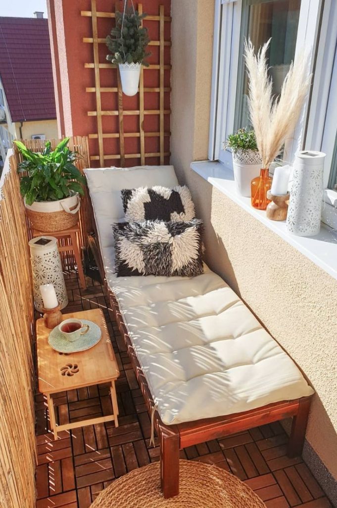 Small balcony sun lounger with cream cushion, bamboo privacy screen, hanging plant, pampas grass and small wooden side table