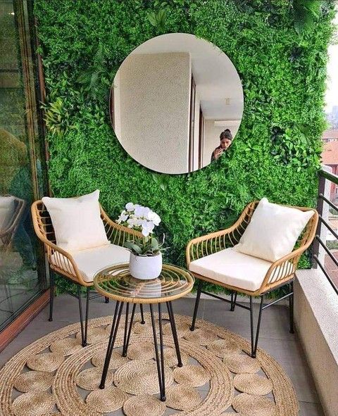 Small balcony with artificial green wall, round mirror, rattan chairs, round jute rug and white orchid
