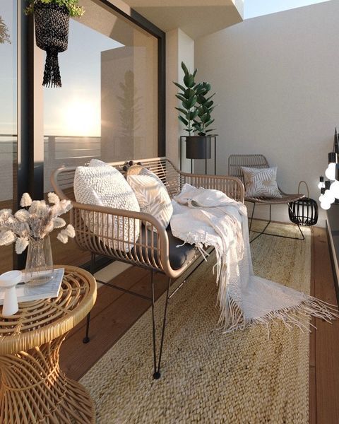Modern boho small balcony with rattan loveseat, knit throw, dried pampas in vase, jute rug at sunset