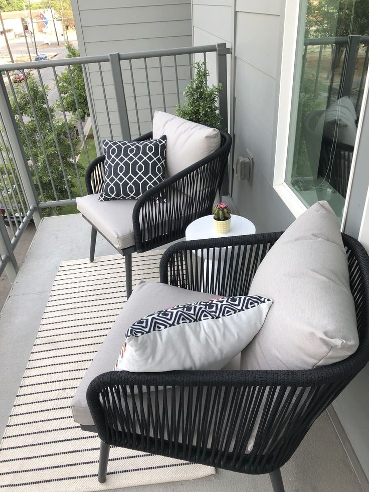 Modern small apartment balcony with black rope chairs, light grey cushions, white stripe rug and small round table