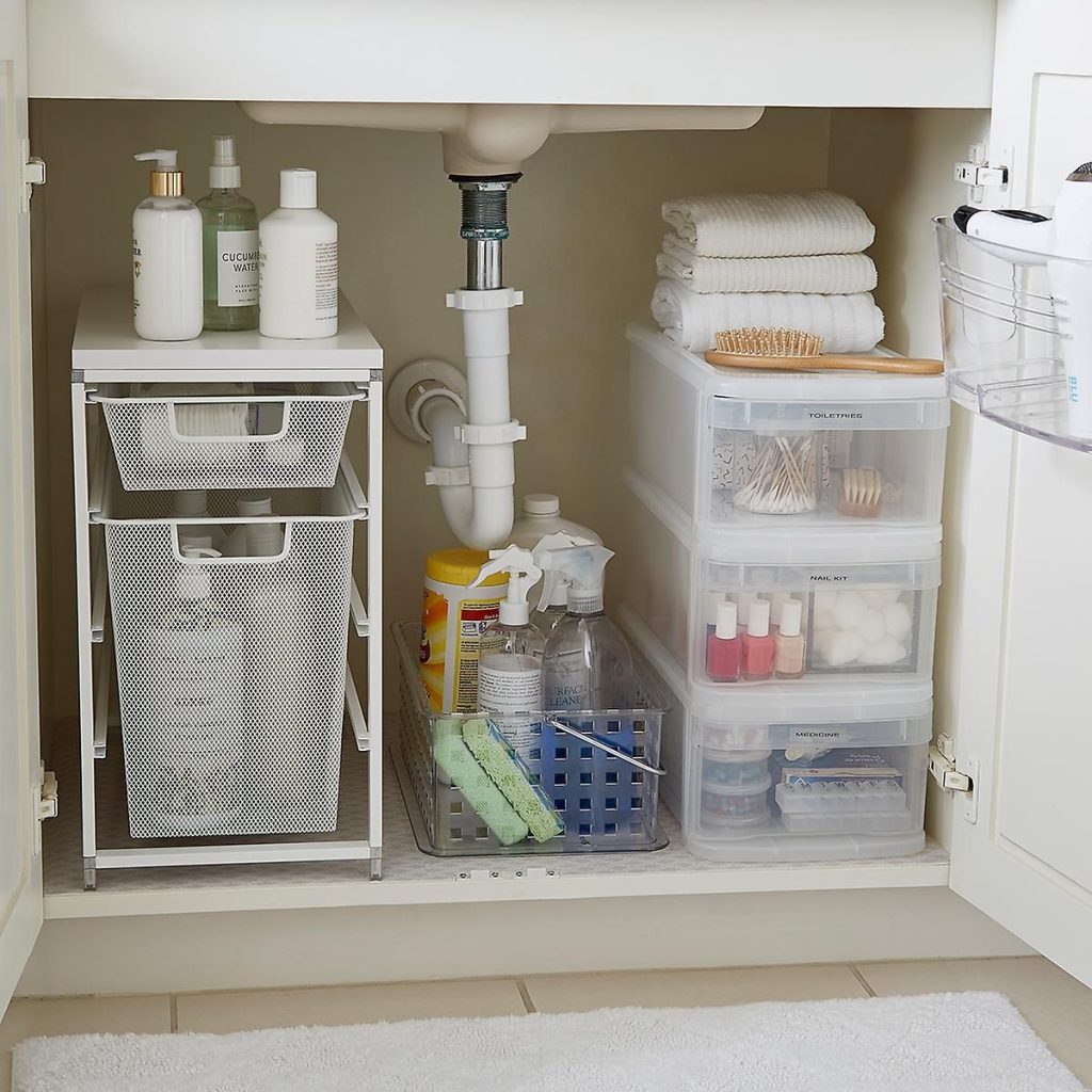 Organized under bathroom sink with a two tier white mesh sliding drawer unit on the left, clear bin with cleaning supplies in the center, and stacked clear labeled drawers for toiletries, nail kit and medicine on the right