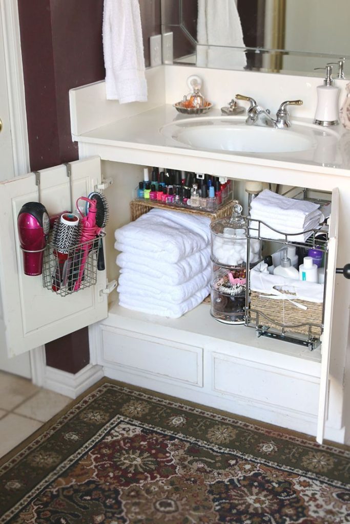 Open bathroom vanity cabinet showing a wire basket mounted on the inside of the door holding a hair dryer, round brush and styling tools