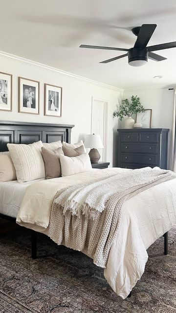 Classic minimalist bedroom with black wood bed frame, cream and tan layered bedding, black ceiling fan, three framed family photos above headboard, and vintage area rug