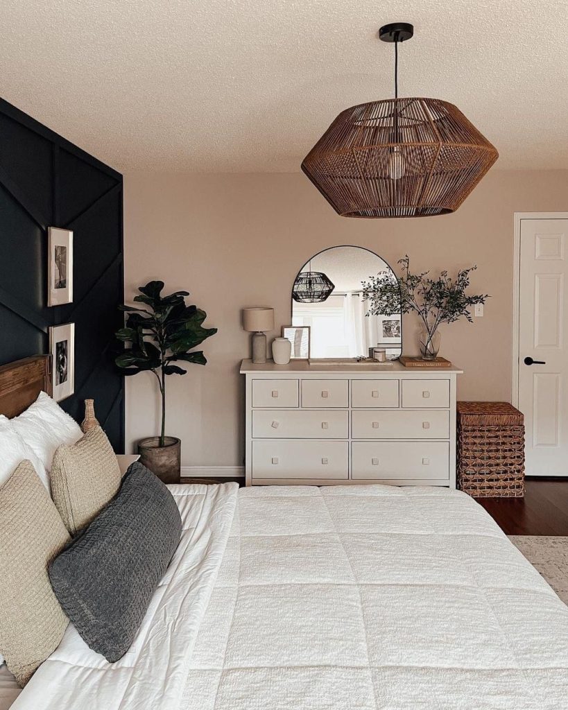 Moody minimalist bedroom with black geometric accent wall, woven rattan pendant light, white dresser styled with round mirror and greenery, fiddle leaf fig, and blush walls
