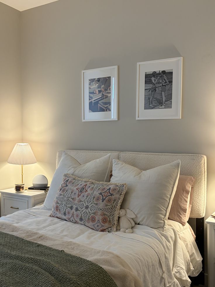 Soft minimalist bedroom with boucle headboard, pleated table lamp, floral accent pillow, and two black and white framed prints on a warm greige wall