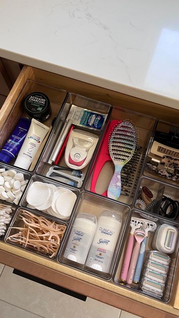 Bathroom vanity drawer organized with clear bins holding cotton rounds, cotton swabs, deodorant, a hairbrush, razors, and daily personal care items