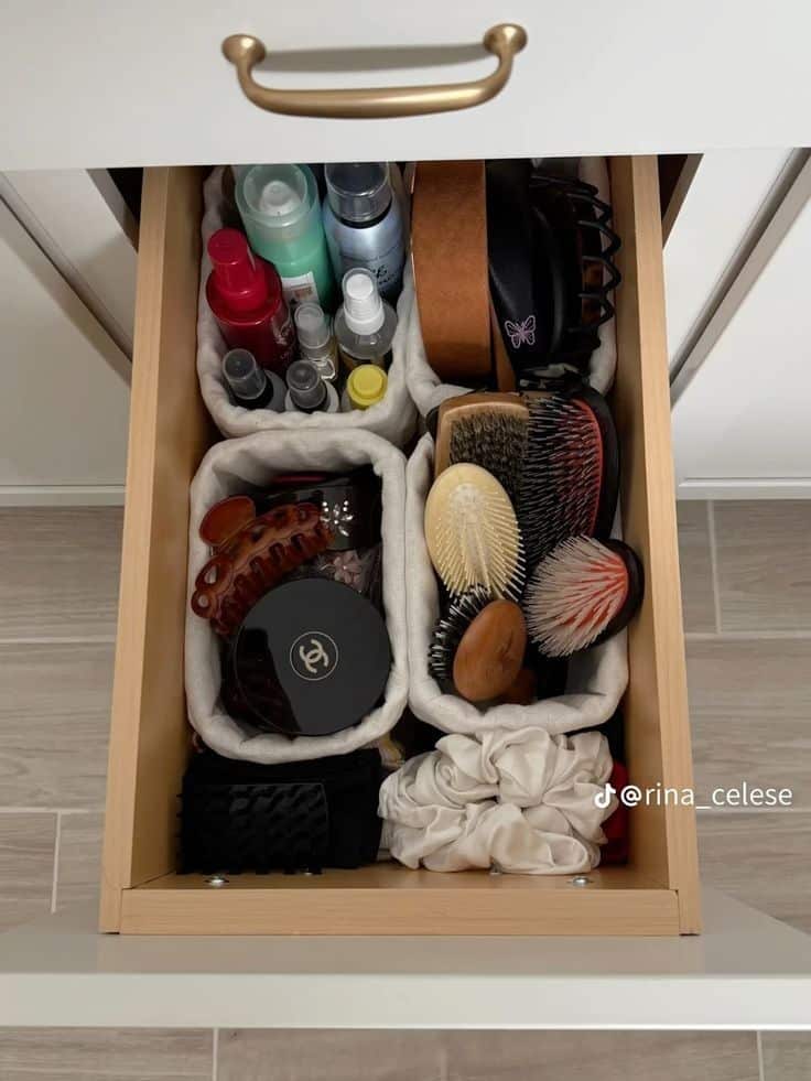 Bathroom drawer with neutral linen fabric baskets organizing hair accessories, brushes, and mini hair care bottles alongside headbands and a compact