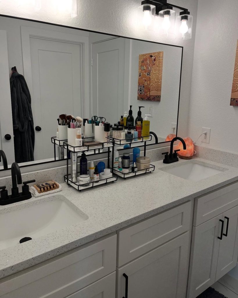 Modern black and white double bathroom vanity with two matching black wire two-tier countertop organizers holding makeup brushes, skincare products, and personal care items for each sink