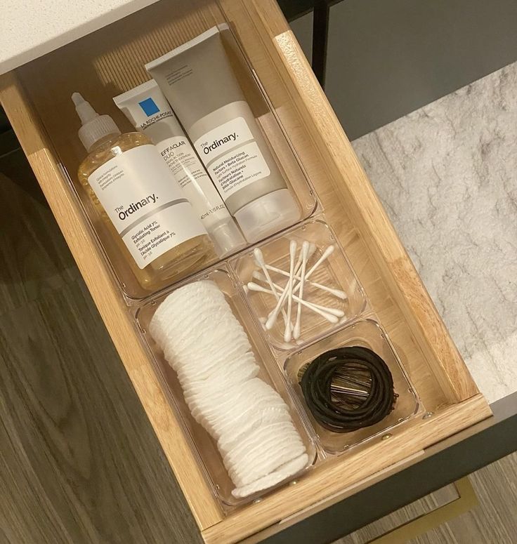 Simple wooden bathroom drawer with clear acrylic organizers holding The Ordinary skincare bottles, cotton pads, cotton swabs, and hair ties