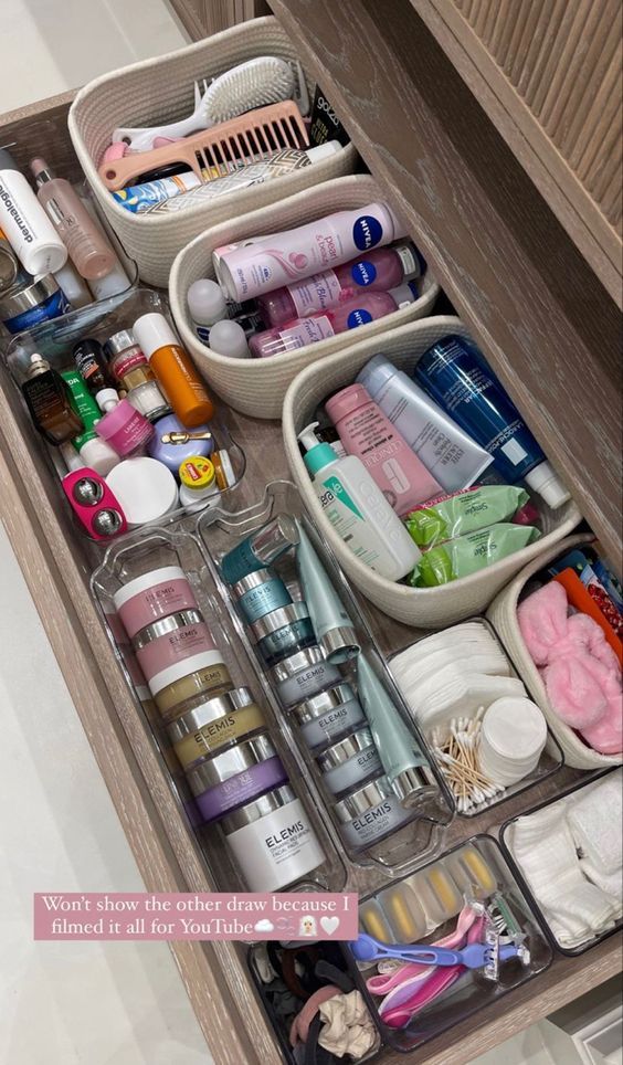 Large bathroom drawer organized with cotton rope baskets holding hair care, body care, and brush tools, alongside clear bins with skincare products and cotton rounds