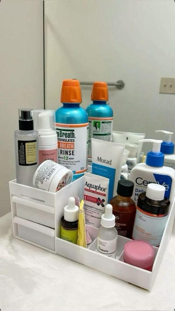 White tiered bathroom countertop organizer holding skincare bottles, serums, face cream, mouthwash, and body lotion in multiple compartments