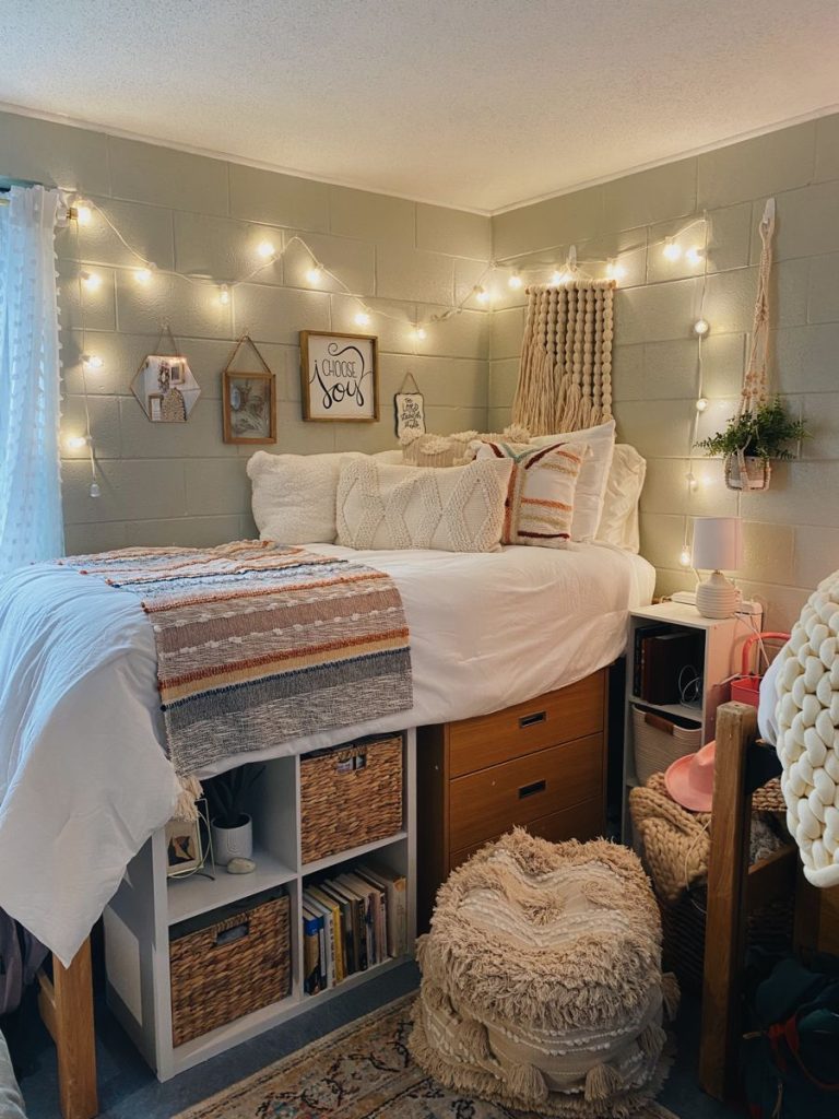 Sage green cinder block dorm room with string lights, macrame, and a fringe pouf