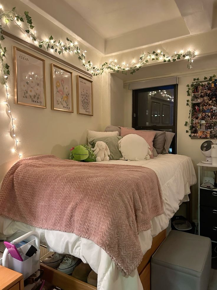 Pink dorm room with faux ivy and string lights along the ceiling edge and gold framed prints