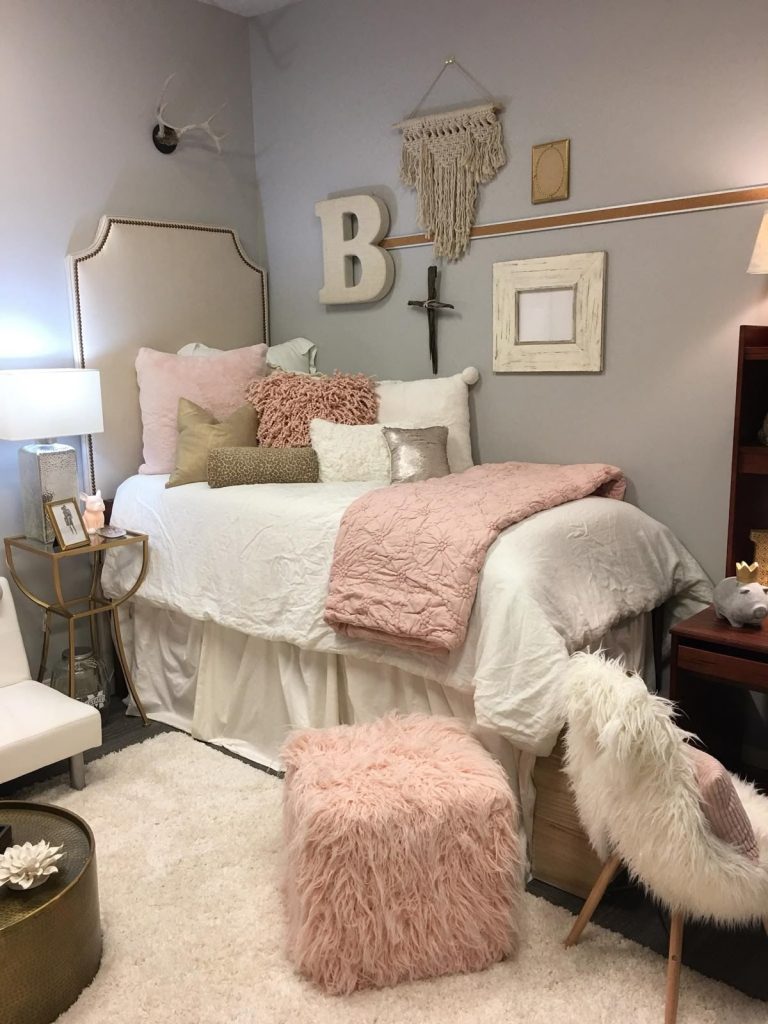 Pink dorm room with a tufted headboard, blush knit throw, and a fluffy pink pouf