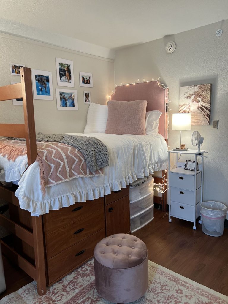 Pink dorm room with a pink upholstered headboard wrapped in string lights