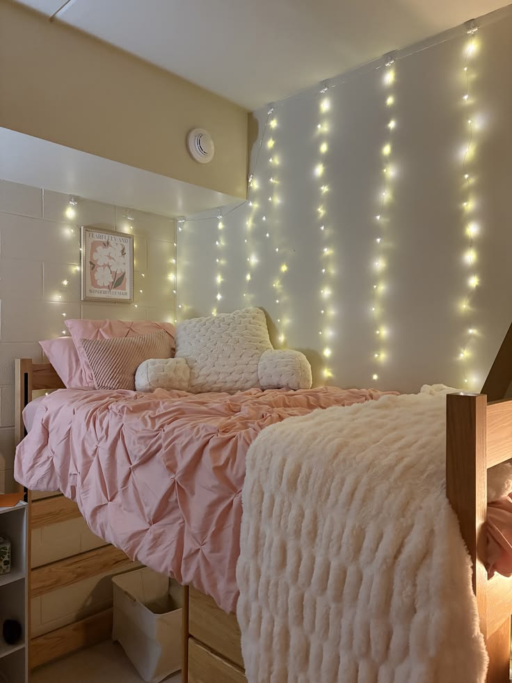 Pink dorm bed with a pinch pleat comforter and vertical curtain fairy lights behind the headboard
