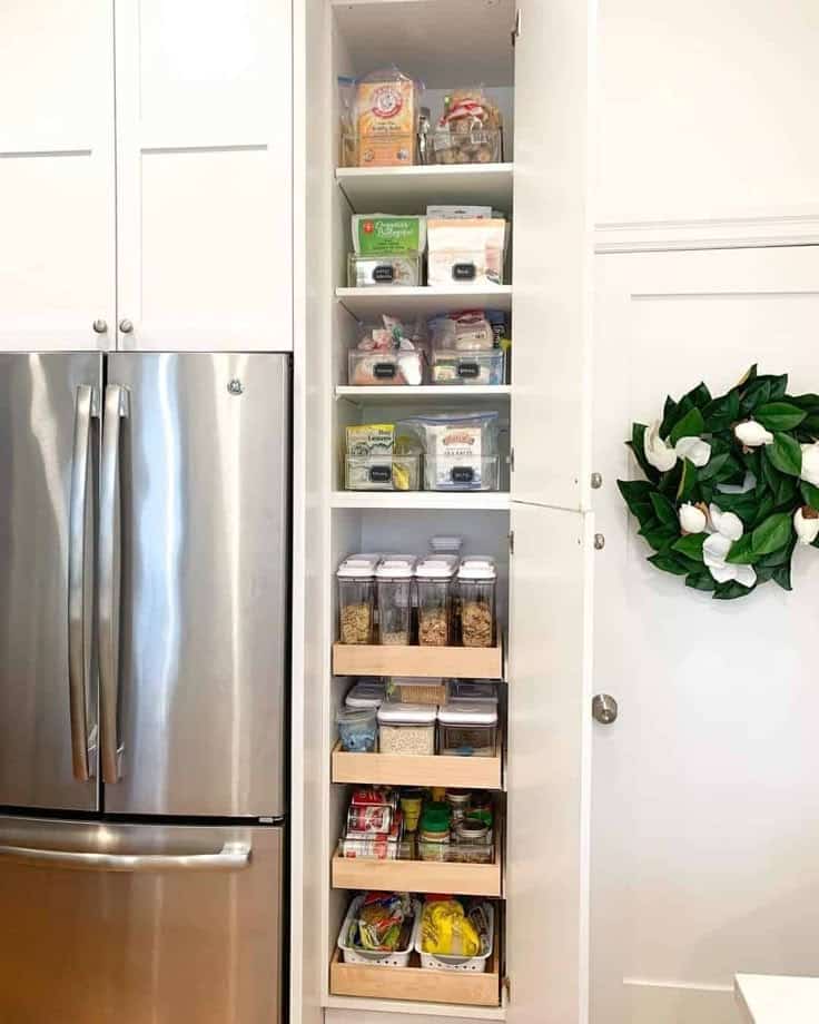 Narrow pantry with slide out wooden trays for canned goods next to refrigerator