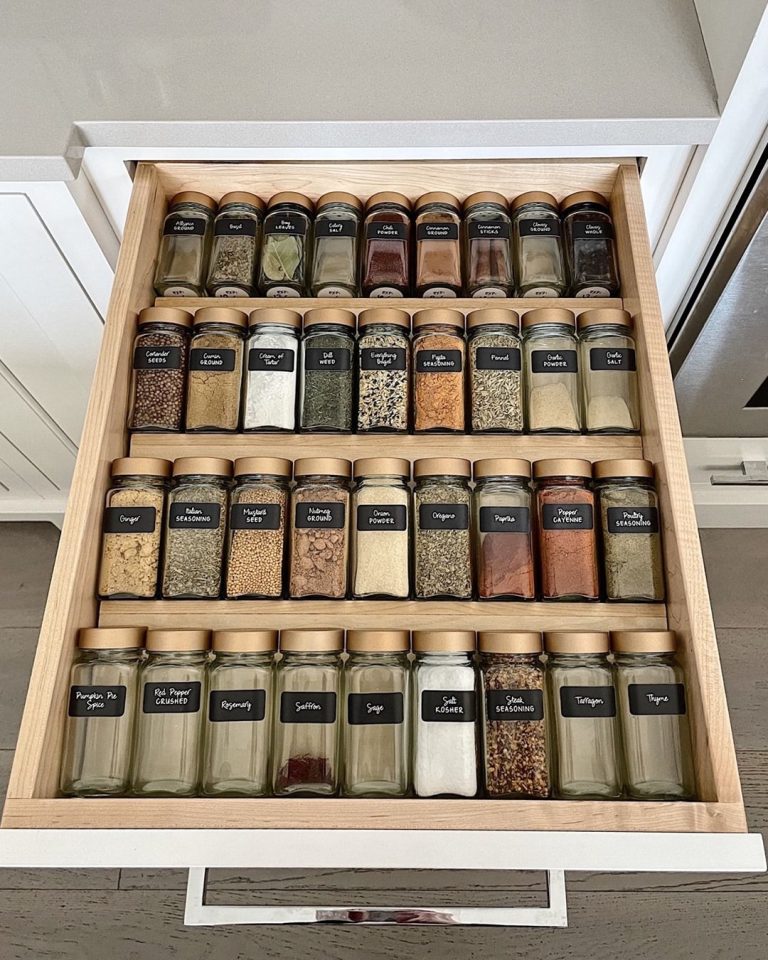 Neatly organised spice drawer with tiered wooden insert and matching glass jars with chalkboard labels, viewed from above.