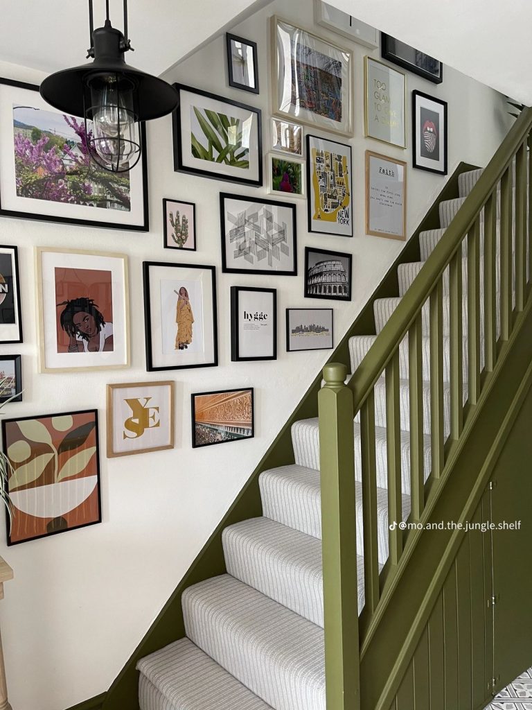Olive green staircase banister with eclectic gallery wall of mismatched prints