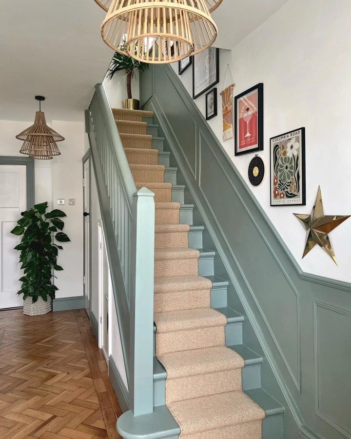 Sage green staircase with paneled walls and gallery wall leading upstairs