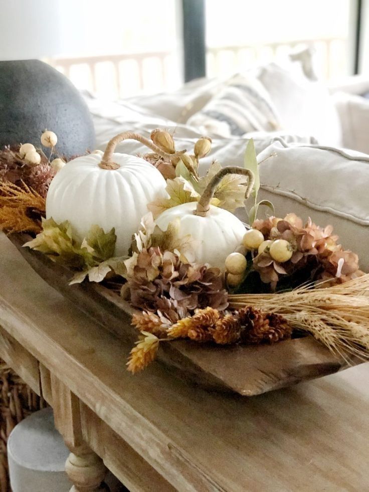 Elegant fall dough bowl with two white pumpkins, dried hydrangea, wheat, pinecones, and gold berries on a wood console.
