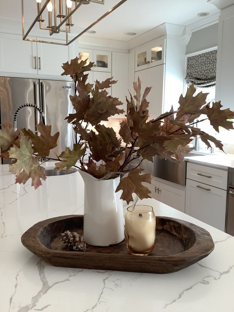 Simple fall dough bowl on a kitchen island with a white pitcher of brown oak leaf branches, an amber candle, and pinecones.