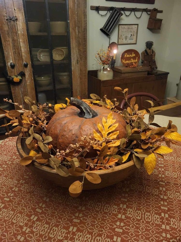 Round wooden fall dough bowl with a single large weathered orange pumpkin surrounded by golden leaves and berry stems.