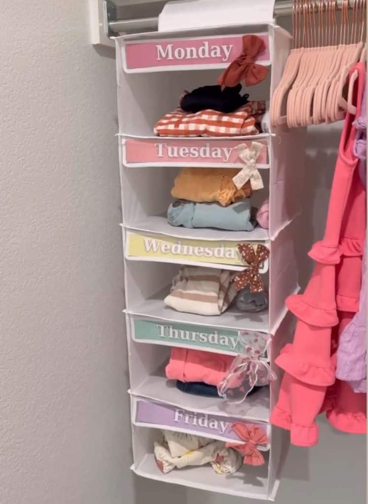 Hanging closet organizer labeled Monday through Friday with folded kids outfits