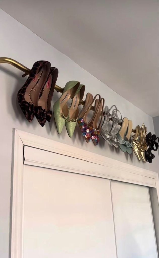 Gold curtain rod mounted above a white closet door holding heels hooked over the rail, including leopard, green, silver, and gold pairs.