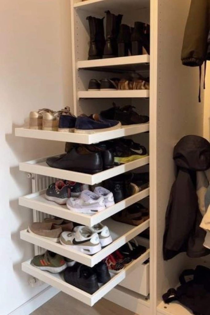 White pull-out shelves extended from inside a wardrobe holding sneakers and loafers, with boots on a fixed shelf above and coats hanging alongside.
