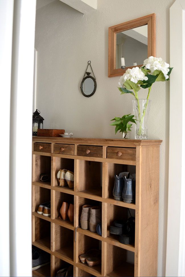 Rustic wooden shoe cubby console with small drawers in a hallway, styled with a vase of white hydrangeas, a lantern, and two mirrors above.