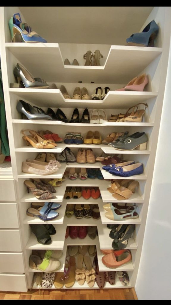 Floor to ceiling white zigzag shelving built into a closet nook, filled with colorful heels, flats, wedges, and sandals.