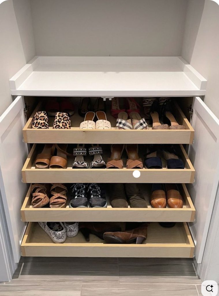Four shallow wooden pull-out drawers inside a white cabinet, holding sandals, mules, heels, and loafers in neat rows.