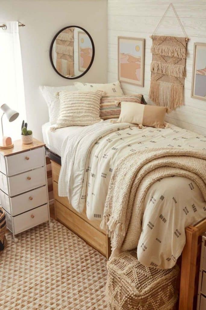 A tan macrame wall hanging adds texture beside a round mirror and desert themed art prints above a neutral bed.