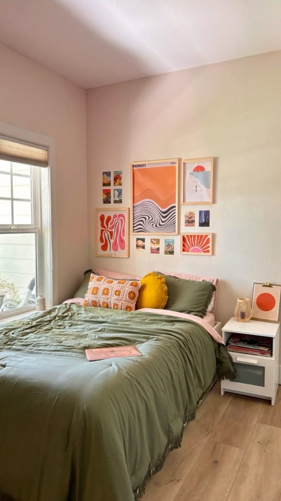 A bold gallery of graphic art prints in orange, pink, and green hangs above a bed with olive green bedding.