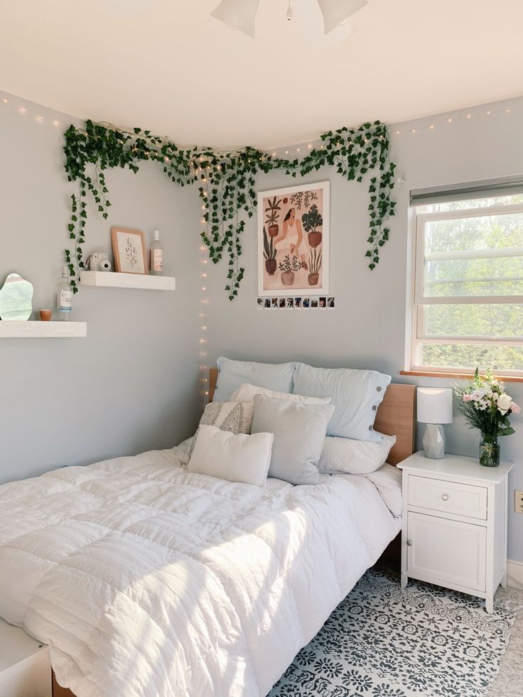 Faux ivy garland trails across the ceiling corner above a bed, paired with string lights and a framed art print.